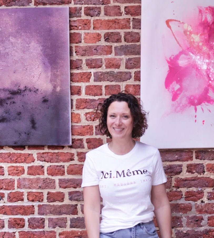 Vanessa Seconde souriante face à la caméra, l'artiste belge est posée devant un mur de briques rouges orné de deux peintures abstraites en teintes de rose et violet.

Portrait devant ses oeuvres abstraites, photographie Vanessa Seconde - Artiste peintre belge

Extrait de son insta: https://www.instagram.com/p/DbTN_dpM9sa/