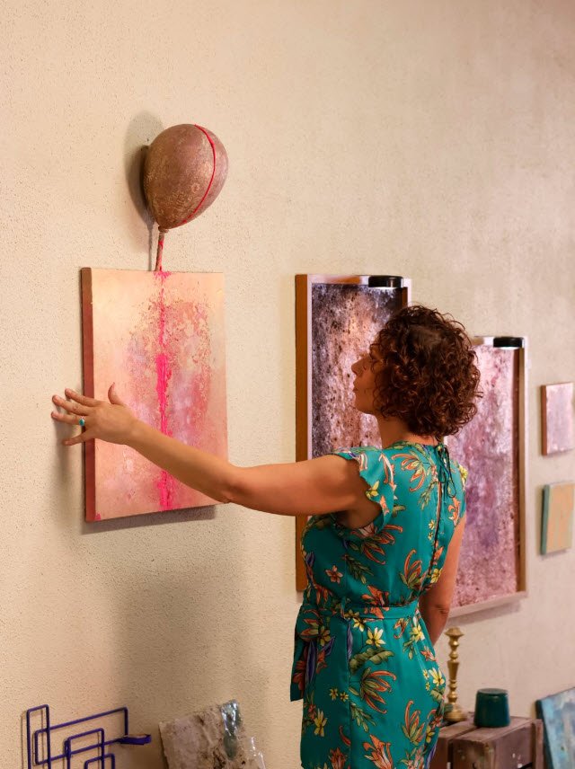 Vanessa Seconde vêtue d'une robe turquoise à motifs floraux installe ses tableaux aux teintes rose et violet, prise de vue de la plasticienne Vanessa Seconde.

Visite d'exposition : découverte des œuvres abstraites de Vanessa Seconde