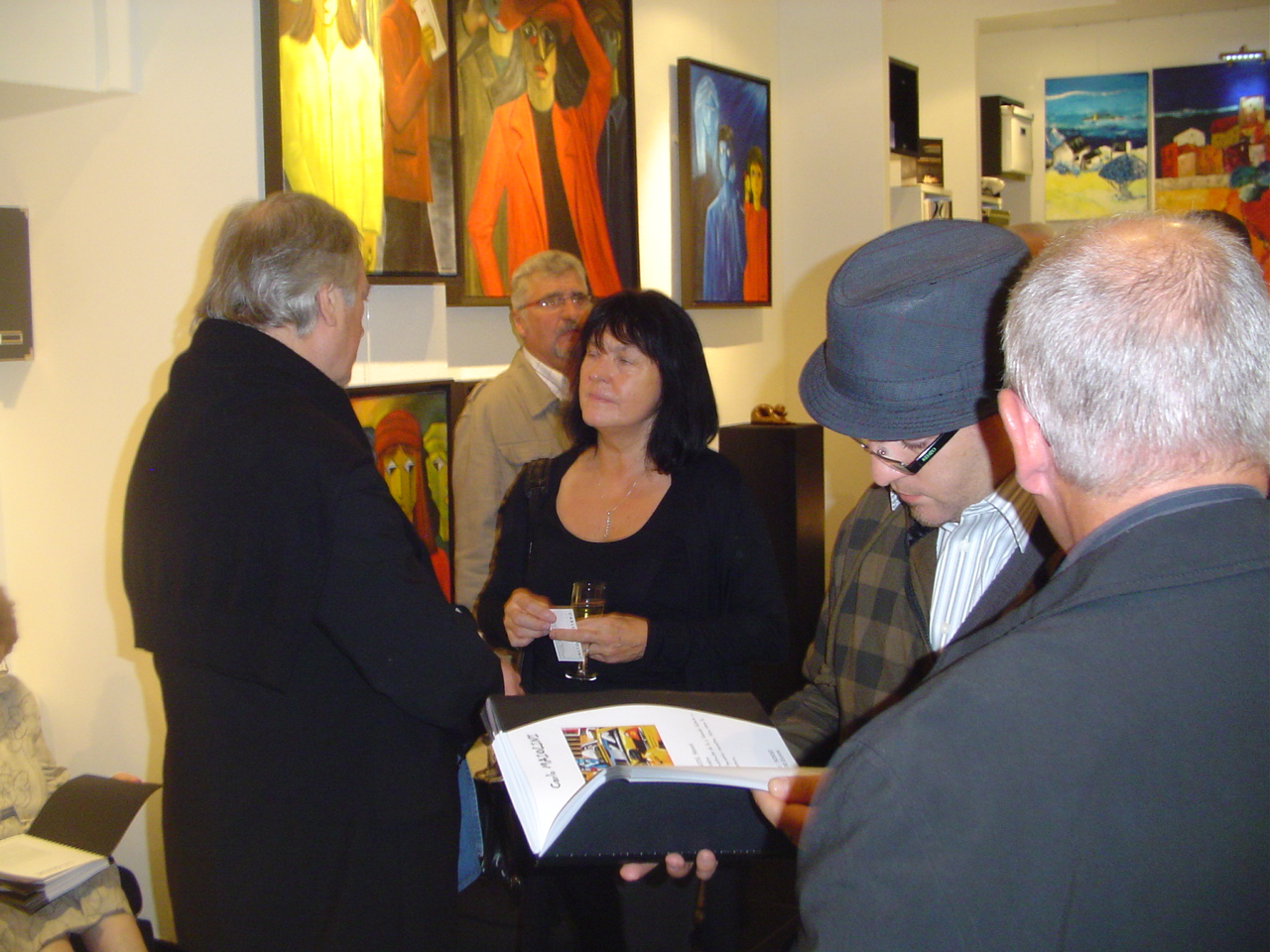 Groupe de visiteurs en conversation devant les oeuvres d'Annie Fontaine. Des toiles aux tonalités chaudes (jaune, orange, rouge) lors d'un vernissage en galerie.