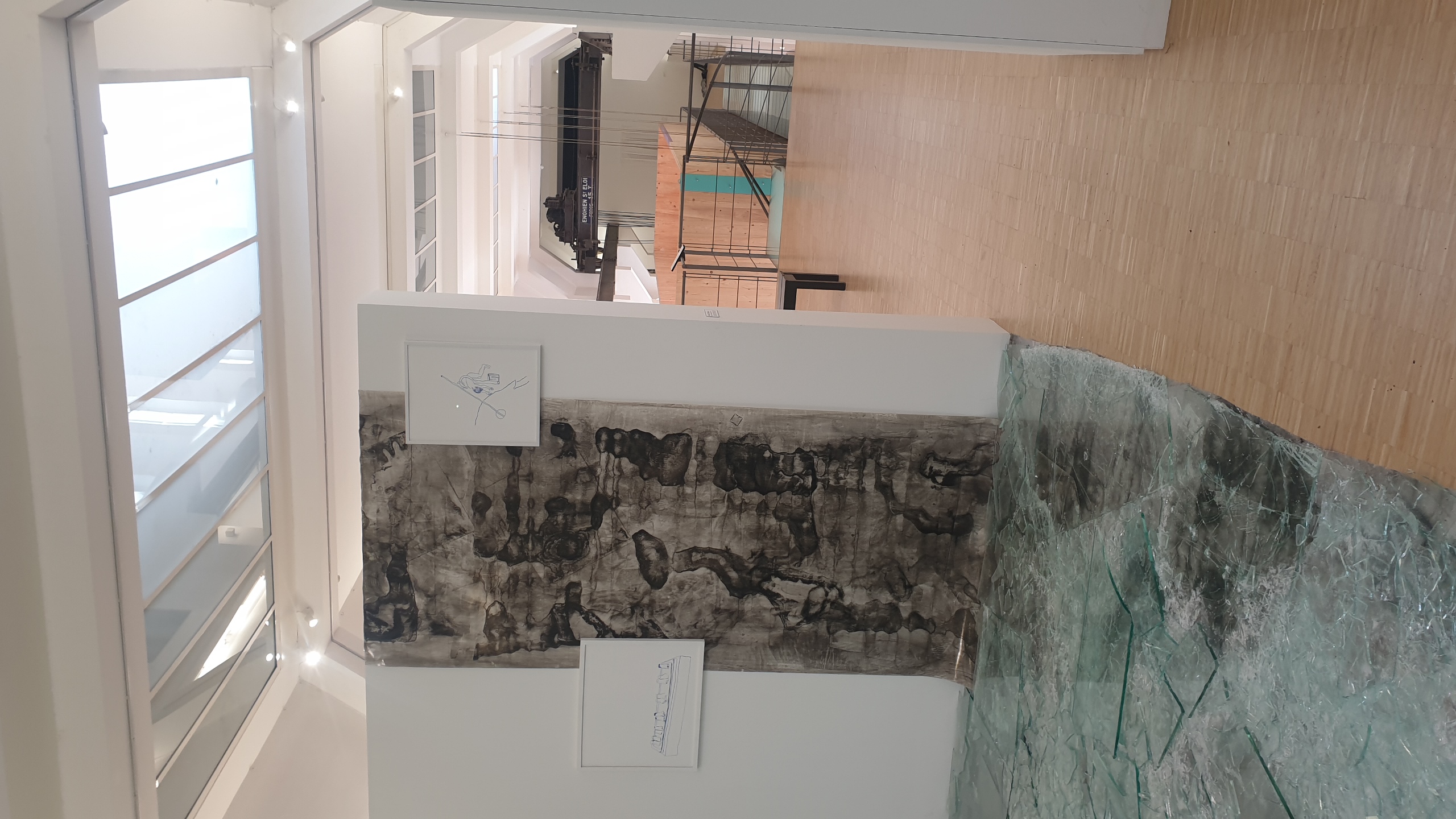Intérieur de la Galerie d'art ISELP à Bruxelles avec des œuvres exposées de l'exposition Haute Nuit : un grand panneau texturé en noir et blanc sur le mur de gauche, des dessins encadrés, une verrière zénithale, et une vue perspective vers d'autres salles.