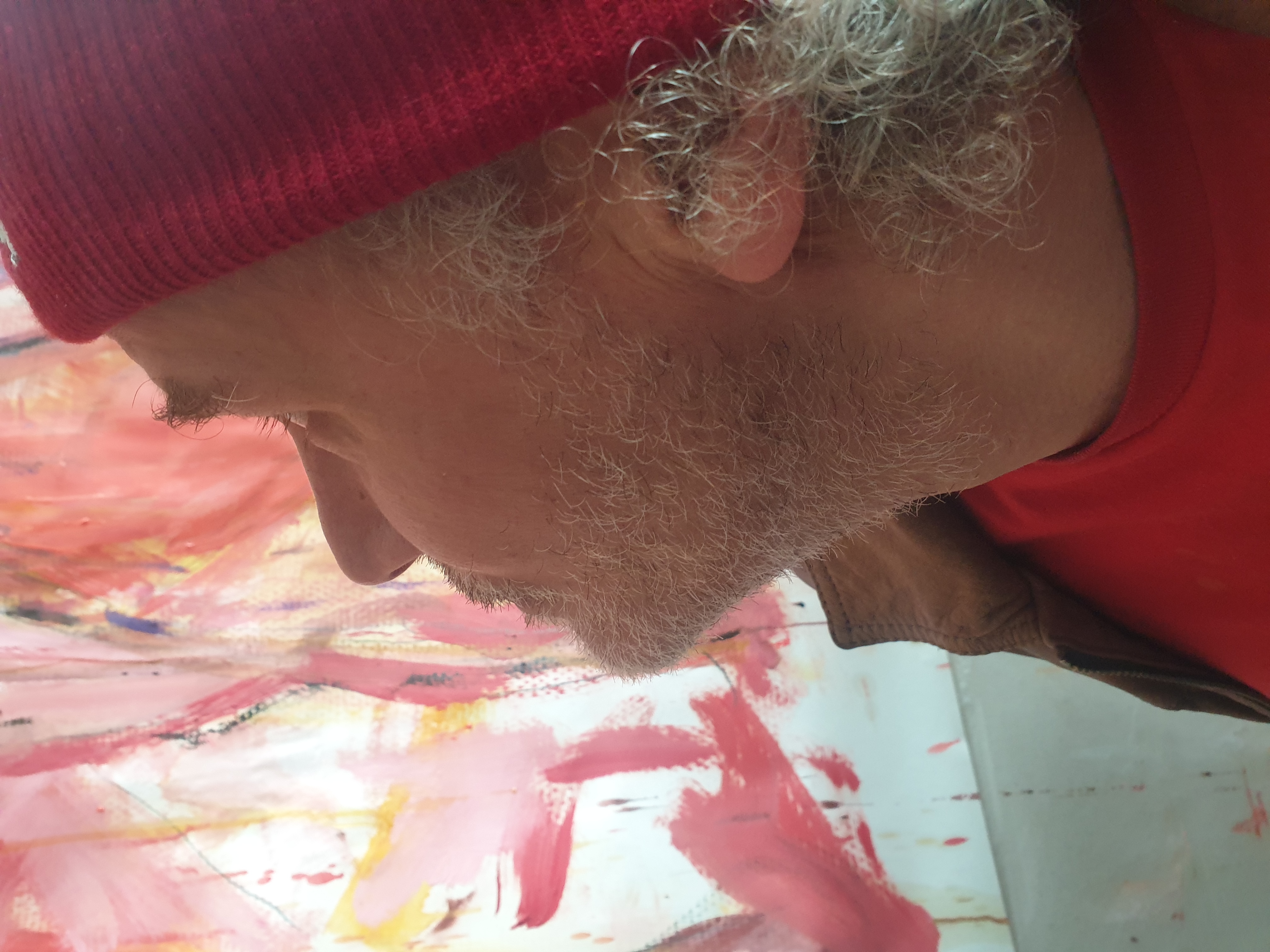 Le plasticien Jérôme Selosse, de profil, observe une peinture abstraite dominée par des teintes roses, blanches et rouges dans son atelier ou galerie.