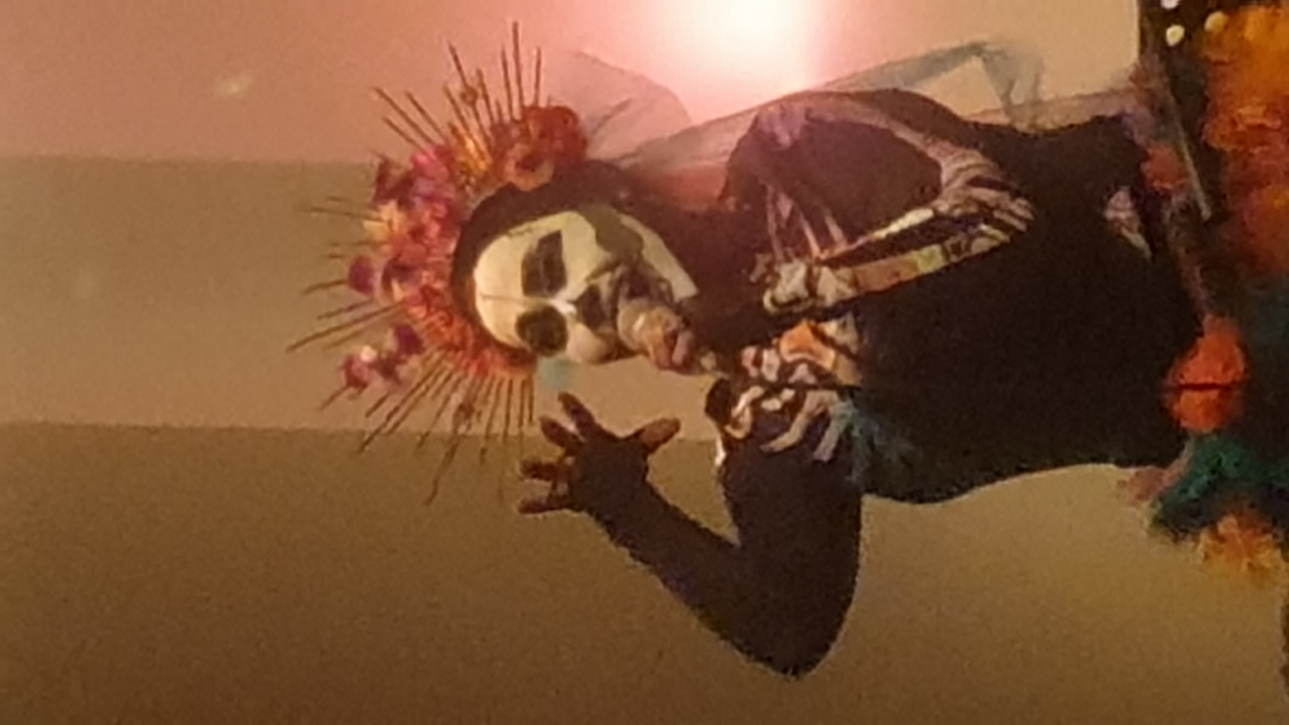 Photographie de Silvia Abalos. Prestation artistique fête des morts Mexicaine. Figure squelettique au masque blanc vêtue de noir, coiffée d'une couronne floral rougeâtre avec nimbe de piques dorées, tenant un microphone, prise par le photographe bruxellois Jérôme Selosse.