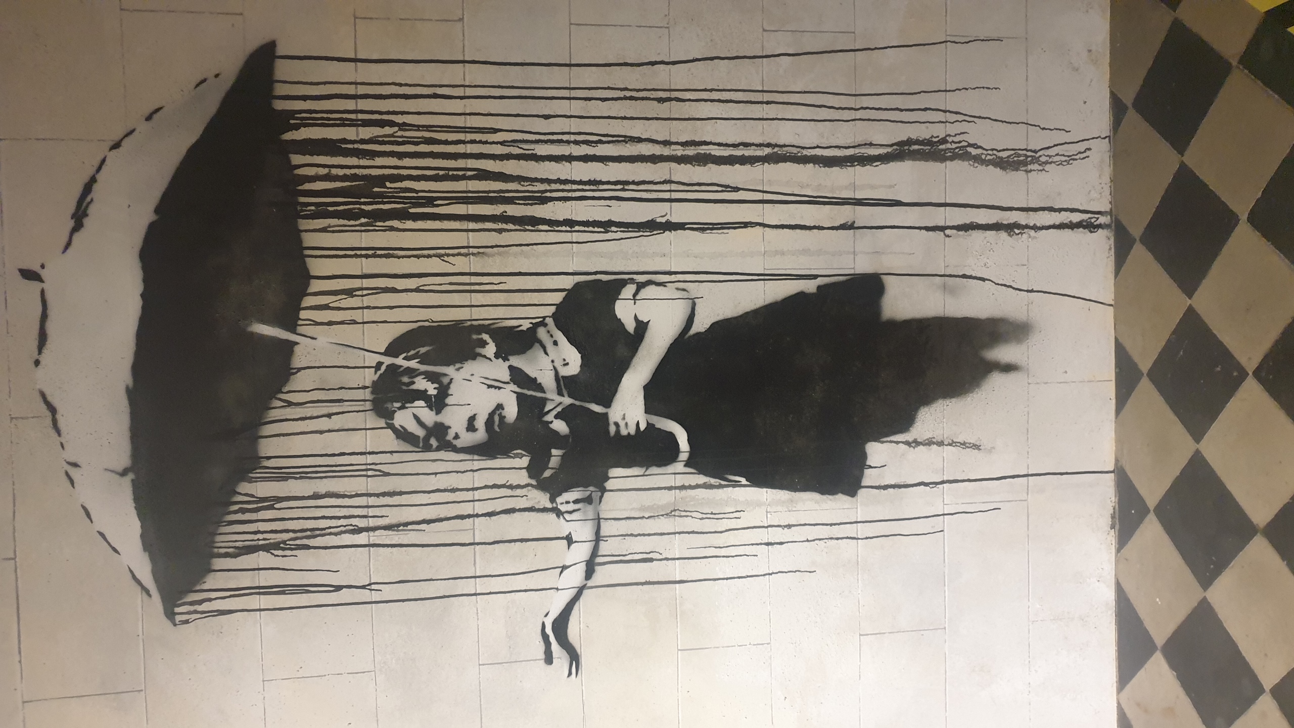 Photographie de Jérôme Selosse au Musée Banksy de Bruxelles : pochoir en noir et blanc sur mur en brique représentant une enfant tenant un parapluie avec de la pluie qui dégouline, technique de stencil bruxelloise.