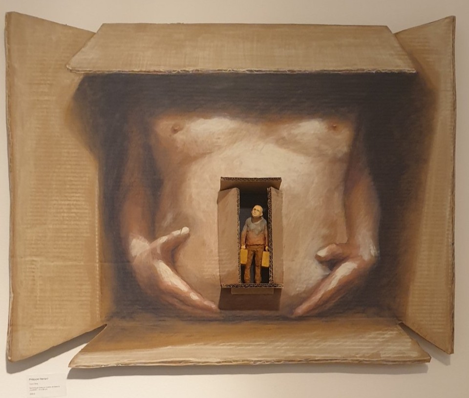 Œuvre en technique mixte sur carton de Philippe Hérard : un torse peint au fond d'un carton ouvert, avec un petit personnage aux valises en son centre.

Le carton s'ouvre comme un petit théâtre. Au fond, un torse nu peint en trompe-l'œil, deux mains posées sur le ventre ; au centre, une seconde boîte abrite un minuscule personnage chauve, une valise dans chaque main. On pense au départ, au déménagement, à la vie qu'on emballe. Une œuvre de Philippe Hérard présentée chez Zaza from Brussels.

« The Working Dead » de Renier Semidey, jusqu'au 15 novembre 2026 chez Zaza from Brussels, rue Blaes 122, 1000 Bruxelles (Marolles). Le mercredi de 11h à 18h, du jeudi au dimanche de 11h à 19h. Entrée libre.

Voir les liens utiles en bas de la description.

🔗 Pour aller plus loin et soutenir l'art local :
L'exposition « The Working Dead » de Renier Semidey : https://dropmuse.art/evenement/the-working-dead-renier-semidey-zazafrombrussels-bruxelles-a9c827
La fiche acteur culturel de Zaza from Brussels : https://dropmuse.art/acteur-culturel/zazafrombrussels
Le site de la galerie : https://zazafrombrussels.com/
Suivre la galerie sur Instagram : https://www.instagram.com/zazafrombrussels/
La galerie sur Facebook : https://www.facebook.com/GalerieZazafromBrussels/
Retrouvez toute l'actualité culturelle sur DROPMUSE : https://dropmuse.art/