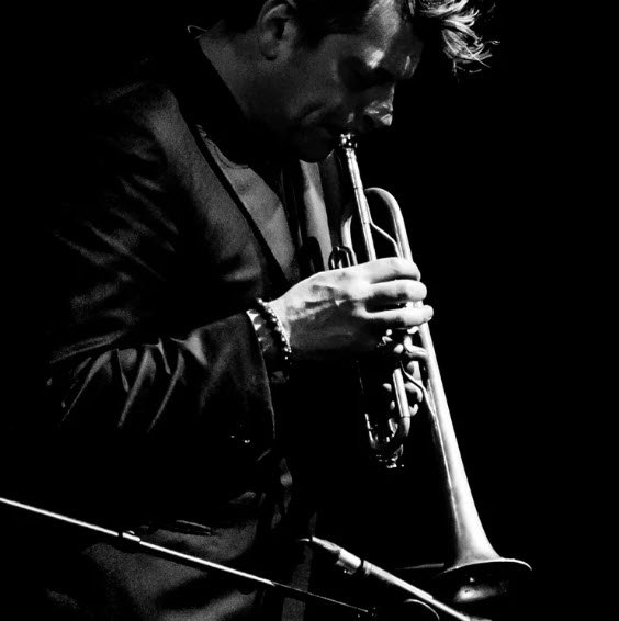 En noir et blanc, Benjamin Biolay joue de la trompette sous un éclairage dramatique, saisi en gros plan lors d'une performance de concert.

Photographie de Lara Herbinia : le trompettiste Benjamin Bioley en concert, série Quand la musique est bonne