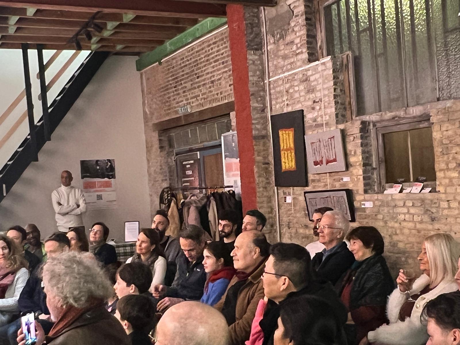 Une foule de visiteurs observe une exposition d'art contemporain dans un espace industriel aux murs de brique, tandis que l'artiste Selosse Art se tient debout à gauche près de ses œuvres et installations murales.