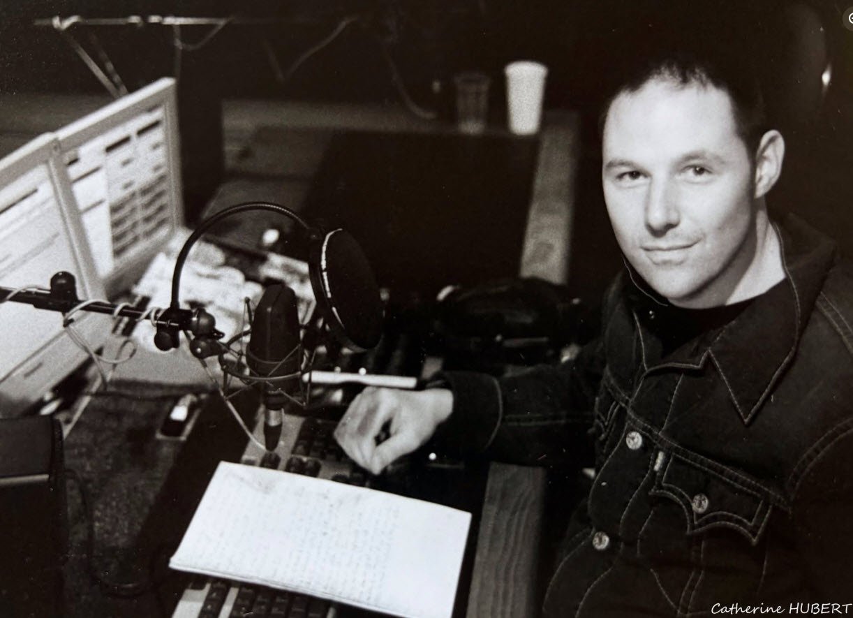 Eric Schmickrath, plasticien, assis devant un microphone et du matériel électronique dans son studio, photographié par Catherine Hubert.