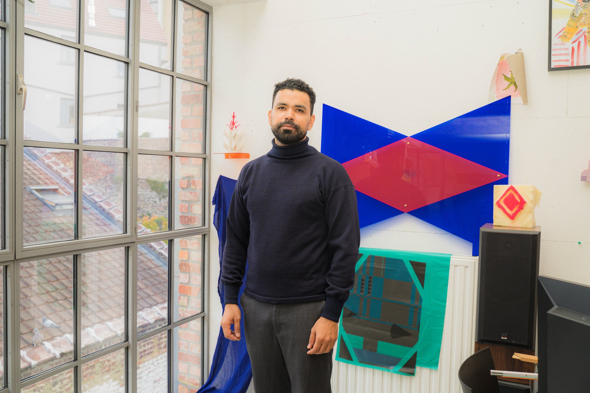 Portrait de l'artiste Badi Rezzak dans son atelier aux KULT XL Ateliers, devant une installation de formes géométriques bleues et rouges. Artiste français originaire d'Algérie, Badi Rezzak mêle sculpture, photographie, installation et performance pour interroger les identités diasporiques, le genre et les assignations raciales. À découvrir aux KULT XL Ateliers 3 (étape n°38), 21a rue Wiertz, le vendredi 6 novembre de 15h à 19h, puis le samedi 7 et le dimanche 8 de 14h à 18h, pendant le Parcours d'Artistes d'Ixelles 2026.

Crédit photo - Gabrielle Liefooghe pour le Parcours d'Artistes d'Ixelles 2026 @googoo.eyes__ @ici_vaisseau_mere

Crédits & Liens :
Instagram : https://www.instagram.com/jean_badi_de_kabylie/
Fiche de l'événement (Dropmuse) : https://dropmuse.art/evenement/parcours-dartistes-dixelles-2026-ateliers-ouverts-creation-locale-ixelles-ixelles-bruxelles
Organisation : Vaisseau Mère — https://www.instagram.com/ici_vaisseau_mere/
Photographe Gabrielle Liefooghe : https://www.gabrielleliefooghe.com/ — https://www.instagram.com/googoo.eyes__/

Kult Ixelles sur DROPMUSE :
https://dropmuse.art/acteur-culturel/kult-ixelles-institution-residence-ixelles