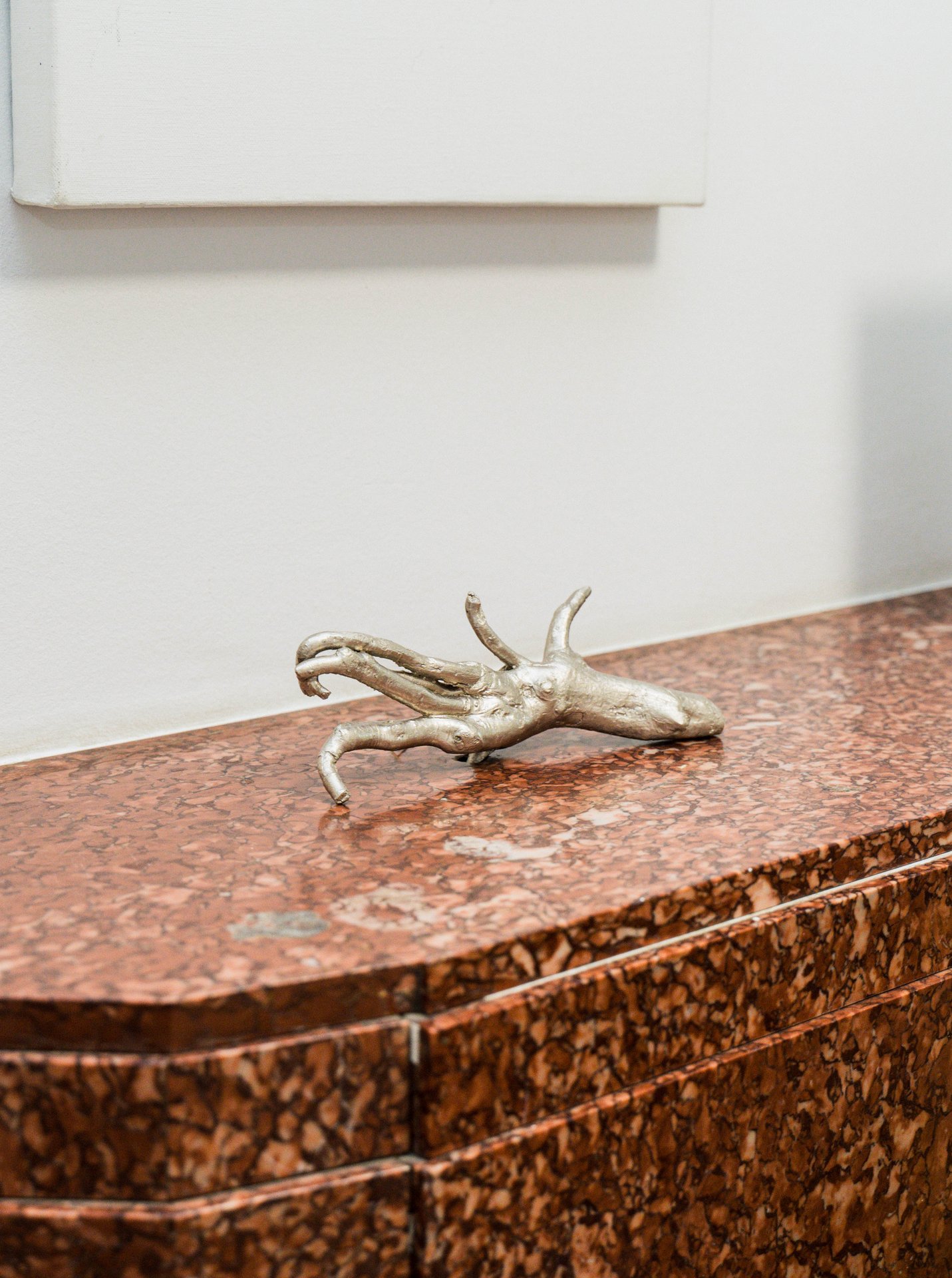 Une petite sculpture de main argentée de Claudine Smal, posée sur un meuble au plateau de marbre rouge. Claudine Smal travaille l'entropie, l'impermanence et les métamorphoses du vivant : par la peinture, la sculpture, la vidéo et l'installation, avec l'or, la pierre ou le textile, elle explore la fragilité, la blessure et la réparation. À découvrir à l'étape n°5 du parcours, 73 rue du Relais, le vendredi 6 novembre de 18h à 22h, puis le samedi 7 et le dimanche 8 de 11h à 18h, pendant le Parcours d'Artistes d'Ixelles 2026.

Crédit photo - Gabrielle Liefooghe pour le Parcours d'Artistes d'Ixelles 2026 @googoo.eyes__ @ici_vaisseau_mere

Crédits & Liens :
Site : https://claudinesmal.be
Instagram : https://www.instagram.com/claudine.smal/
Fiche de l'événement (Dropmuse) : https://dropmuse.art/evenement/parcours-dartistes-dixelles-2026-ateliers-ouverts-creation-locale-ixelles-ixelles-bruxelles
Organisation : Vaisseau Mère — https://www.instagram.com/ici_vaisseau_mere/
Photographe Gabrielle Liefooghe : https://www.gabrielleliefooghe.com/ — https://www.instagram.com/googoo.eyes__/

Kult Ixelles sur DROPMUSE :
https://dropmuse.art/acteur-culturel/kult-ixelles-institution-residence-ixelles