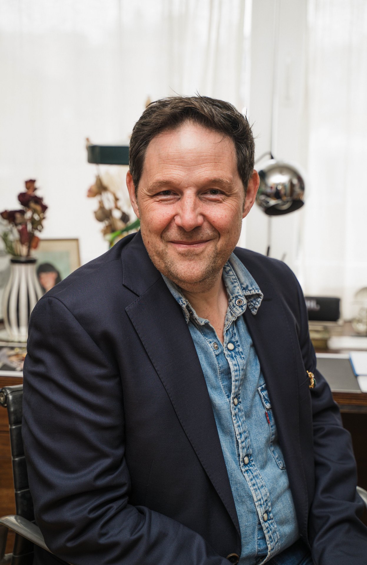 Portrait souriant du plasticien Eric Schmickrath, veste bleu marine et chemise en jean, dans son intérieur entre fleurs séchées et lampe chromée. Originaire d'Arlon et installé à Bruxelles depuis 1995, Eric Schmickrath assemble plumes, papier et coquilles d'œuf en collages peuplés de figures oniriques, drôles ou mélancoliques, au regard interrogateur. À découvrir chez SELOSSE ART, 22 avenue Armand Huysmans, dans l'exposition collective de six artistes belges, le vendredi 6 novembre de 18h à 22h, le samedi 7 de 12h à 20h et le dimanche 8 de 10h à 17h, pendant le Parcours d'Artistes d'Ixelles 2026.

Crédit photo - Gabrielle Liefooghe pour le Parcours d'Artistes d'Ixelles 2026 @googoo.eyes__ @ici_vaisseau_mere

Crédits & Liens :
Sa fiche DROPMUSE : https://dropmuse.art/artiste/eric-schmickrath-plasticien-bruxelles
Site : https://ericleyders.wixsite.com/website
L'exposition collective : https://dropmuse.art/evenement/exposition-collective-de-6-artistes-belges-a-ixelles-bruxelles-parcours-dartistes-2026-selosse-art-2
Fiche de l'événement (Dropmuse) : https://dropmuse.art/evenement/parcours-dartistes-dixelles-2026-ateliers-ouverts-creation-locale-ixelles-ixelles-bruxelles
Organisation : Vaisseau Mère — https://www.instagram.com/ici_vaisseau_mere/
Photographe Gabrielle Liefooghe : https://www.gabrielleliefooghe.com/ — https://www.instagram.com/googoo.eyes__/

Kult Ixelles sur DROPMUSE :
https://dropmuse.art/acteur-culturel/kult-ixelles-institution-residence-ixelles