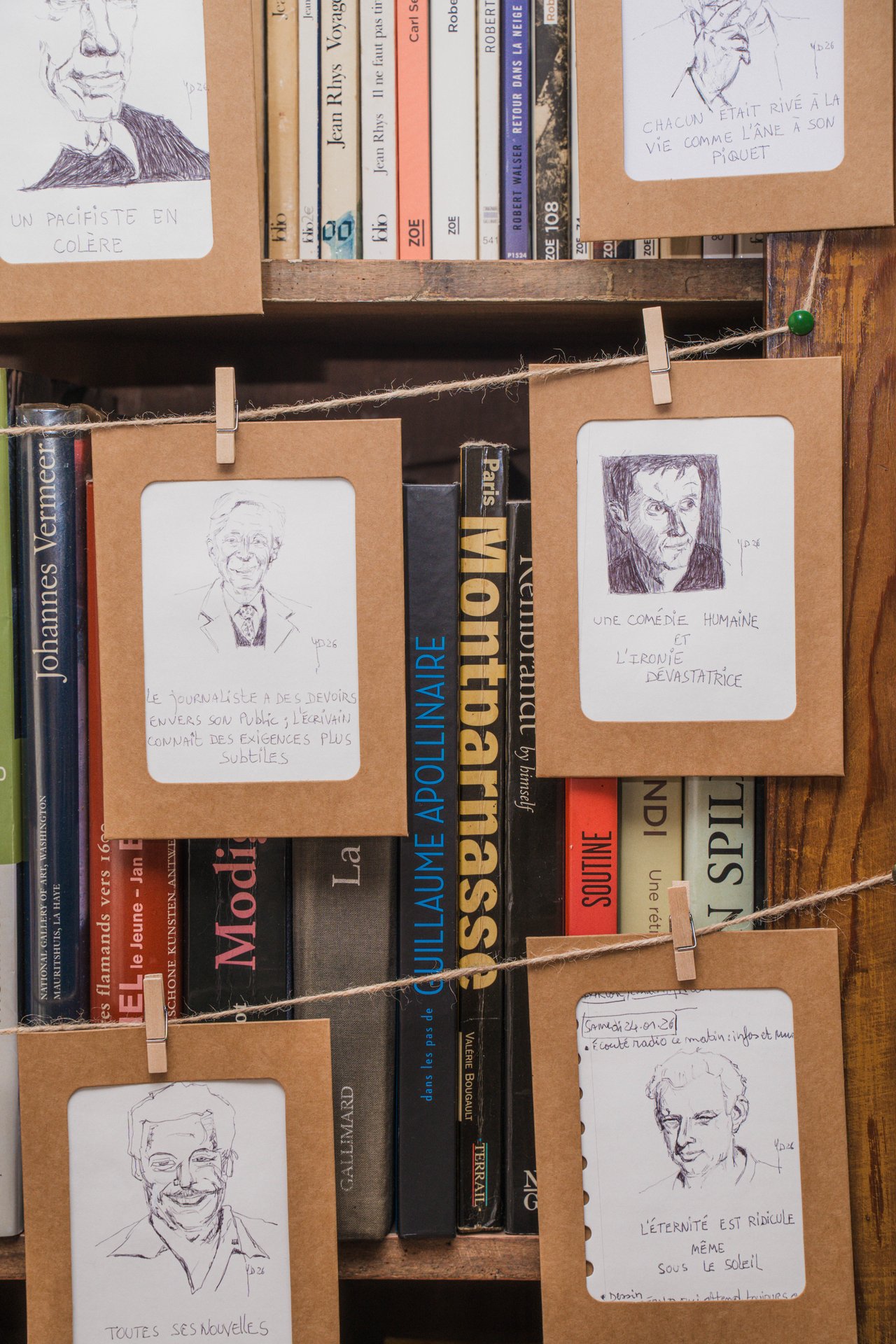 Gros plan sur les portraits miniatures d'Yves Delbar, tendus sur une ficelle devant les livres de sa bibliothèque. Nouvelliste et dessinateur, Yves Delbar expose 60 miniatures au feutre inspirées de haïkus et 150 mini-portraits au bic noir, au format 10 x 12 cm. À découvrir à l'étape n°43 du parcours, 23 rue Jules Bouillon (3e étage), le vendredi 6 novembre de 18h à 22h, puis le samedi 7 et le dimanche 8 de 11h à 18h, pendant le Parcours d'Artistes d'Ixelles 2026.

Crédit photo - Gabrielle Liefooghe pour le Parcours d'Artistes d'Ixelles 2026 @googoo.eyes__ @ici_vaisseau_mere

Crédits & Liens :
Fiche de l'événement (Dropmuse) : https://dropmuse.art/evenement/parcours-dartistes-dixelles-2026-ateliers-ouverts-creation-locale-ixelles-ixelles-bruxelles
Organisation : Vaisseau Mère — https://www.instagram.com/ici_vaisseau_mere/
Photographe Gabrielle Liefooghe : https://www.gabrielleliefooghe.com/ — https://www.instagram.com/googoo.eyes__/

Kult Ixelles sur DROPMUSE :
https://dropmuse.art/acteur-culturel/kult-ixelles-institution-residence-ixelles