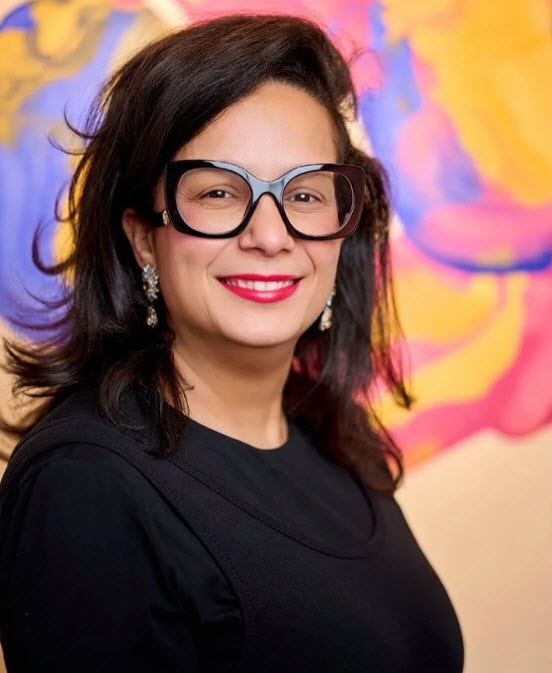 Portrait de Saloua SARHIRI Bruxelles. Cheveux mi-longs, lunettes carrées et un haut noir, souriante face à la caméra devant un fond abstrait aux teintes rose, jaune et bleu. Représentant « The Embrace of Solar Souls »
A silent dance of light and color…
🌸 Pink for tenderness
💙 Blue for dreams
🌞 Yellow for eternal mornings
✨ Gold for the memory of a star never forgotten
A sacred union, a breath between two souls.
Not a form, but a feeling.
Not an image, but a vibration.
A gentle offering to the heart.
