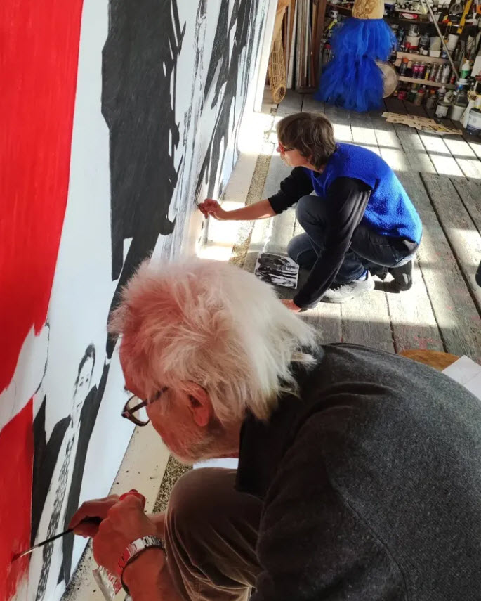 Christian Rolet et Véronique Poppes peignent une grande toile en blanc et noir avec des touches de rouge vif dans un atelier lumineux rempli de matériel artistique. Photographie Christian Rolet. Action Painting.