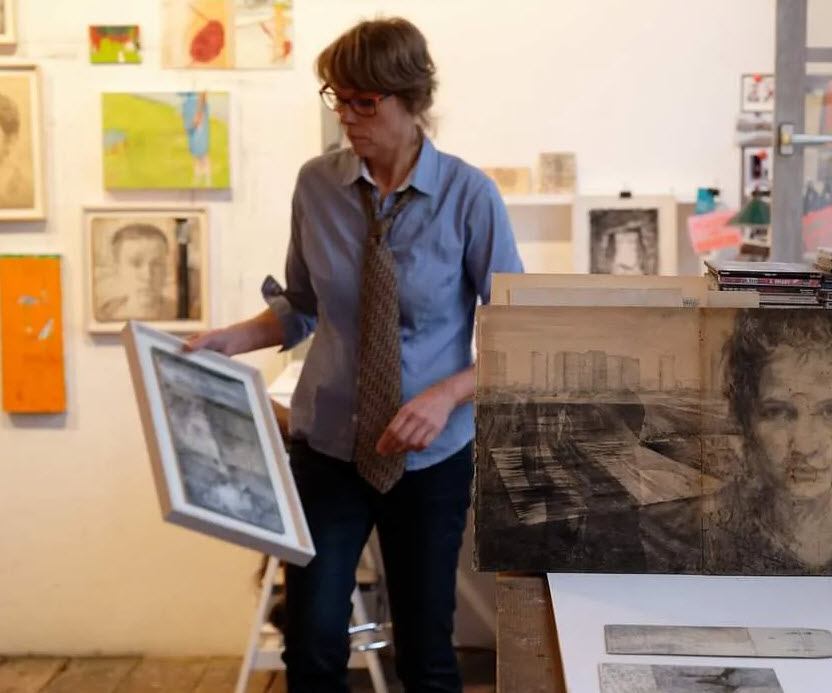 Véronique Poppe , l'artiste plasticienne belge dans son atelier rempli d'œuvres accrochées au mur et d'archives visuelles empilées sur une table.