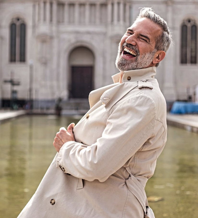 Portrait de Olivier Figus Lechevalier, comédien, souriant face à la caméra en trench-coat beige clair, posé de trois quarts devant une architecture classique avec un plan d'eau en arrière-plan.

Rire c’est la vie!
Rire c’est être libre!
Rire c’est être heureux !

Let’s spread LOVE!