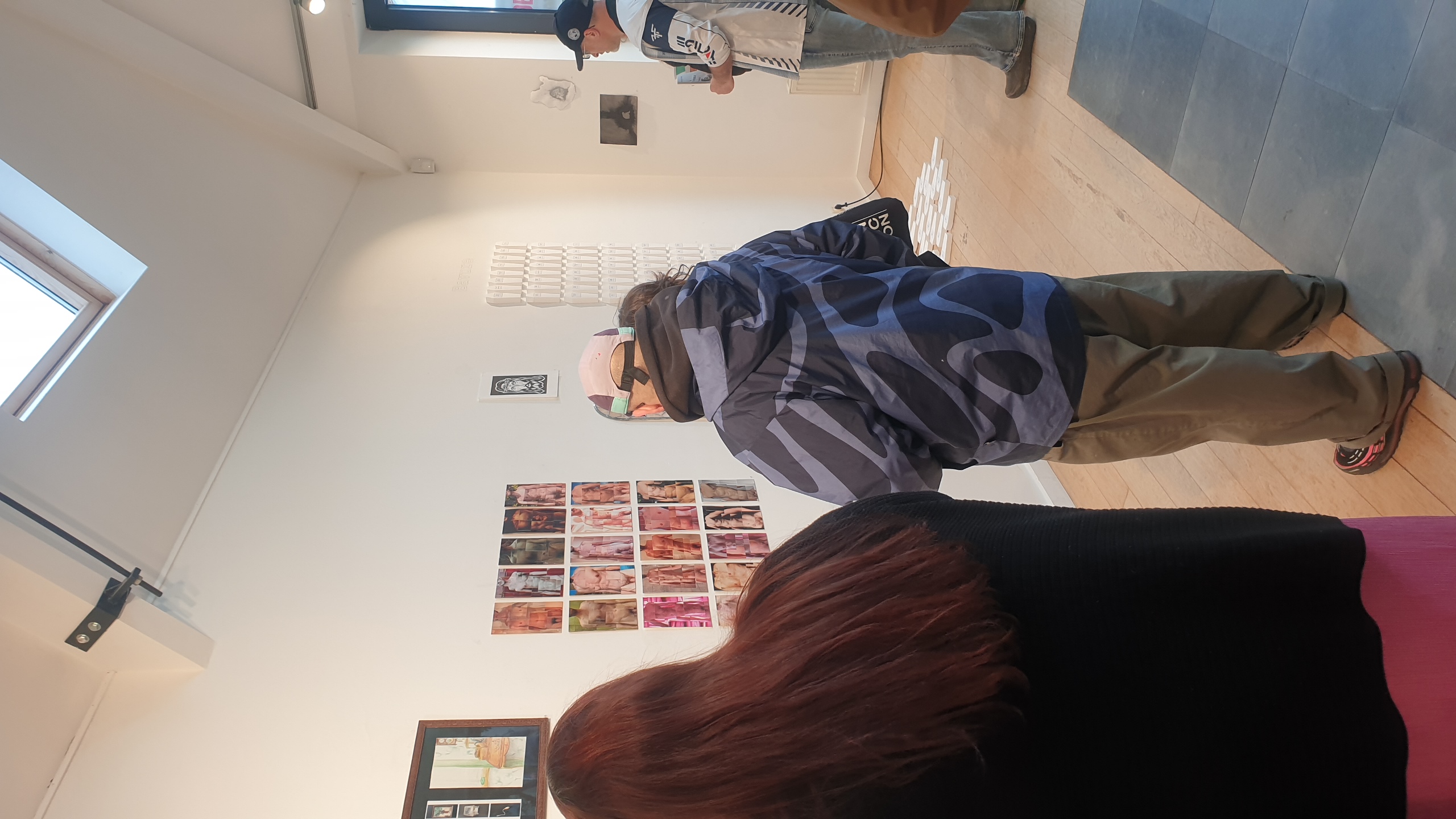 Des visiteurs observent des œuvres d'art colorées accrochées aux murs d'une galerie lumineuse, incluant une série de petits tableaux et diverses pièces du collectif artistique Galerie Vertige basé à Bruxelles. Evènement couvert par dropmuse.art