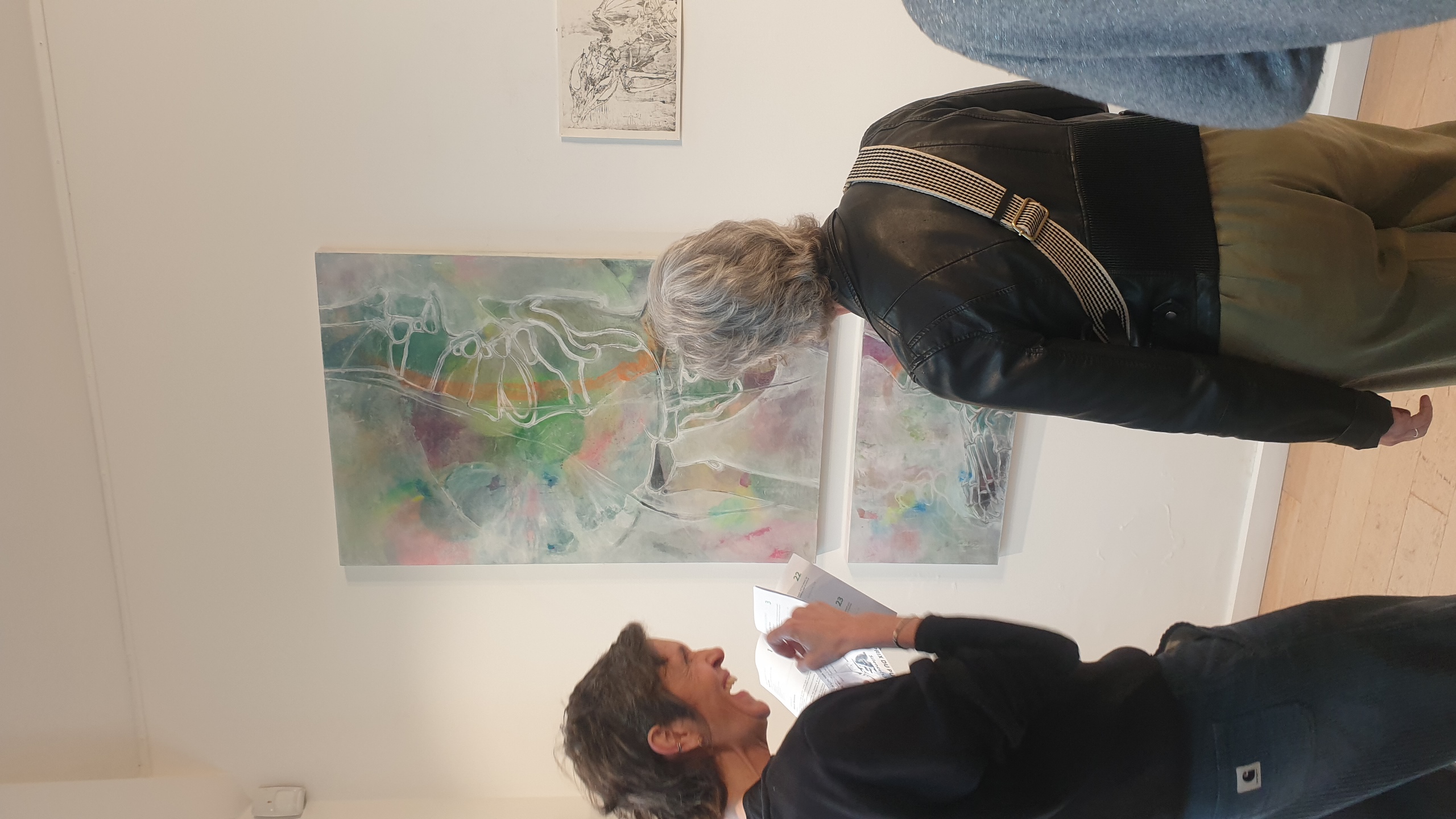 Deux visiteurs examinent une peinture abstraite aux teintes pastel avec des tracés blancs organiques, exposée dans une galerie blanche minimaliste.