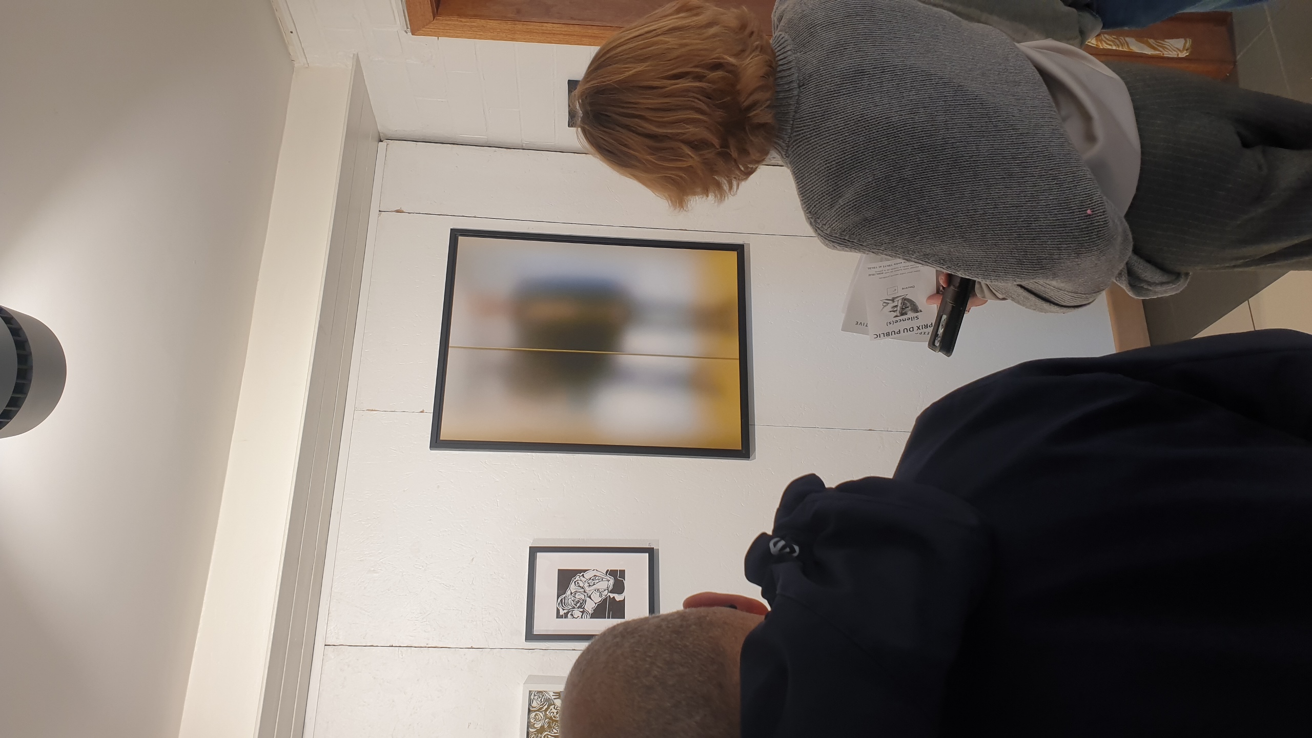 Deux visiteurs de dos contemplent une peinture abstraite aux teintes jaunes et bleues dans une galerie blanche minimaliste, document informatif à la main. Infos pratiques :
📅 Exposition collective "Silence(s)" : du 12 juin au 8 juillet 2026
📍 Galerie Vertige — Rue de Veeweyde 60, 1070 Anderlecht (Bruxelles)