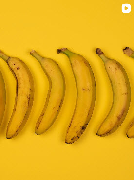 Cinq bananes jaunes alignées horizontalement sur un fond jaune vif, photographie minimaliste.